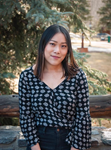 A person wearing a patterned blouse poses in front of a wooden fence with trees in the background.