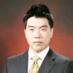 A man in a suit and striped tie poses against a dark red background.