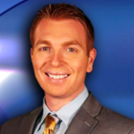 A man in a suit and tie smiles against a blue gradient background.