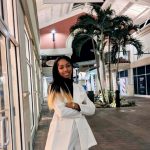 Person in a white suit stands with arms crossed outside a store called "Closet Freekz" in a mall walkway with palm trees.