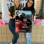 Two women pose smiling, holding a large magazine cover with an image of a chef. A banner in the background reads "The Future Is Female.