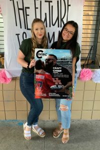 Two women pose smiling, holding a large magazine cover with an image of a chef. A banner in the background reads "The Future Is Female.