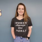 Person standing against a wall, wearing a shirt that reads "Women change the world.