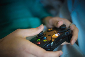 Person holding a black gaming controller with colorful buttons, focused on playing a video game.