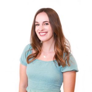 A person with long brown hair, wearing a light blue top, smiles against a white background.