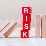 Red blocks spelling "RISK" prevent wooden blocks from toppling, illustrating risk management and barrier concept.