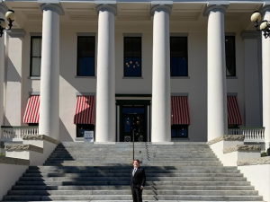 A person stands on the steps in front of a large building with tall columns and red-striped awnings.