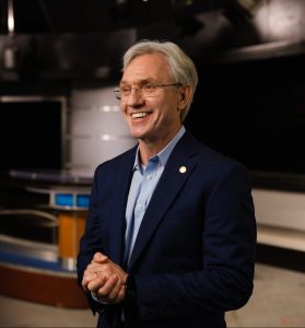 Man in a suit smiling while standing in a studio environment.