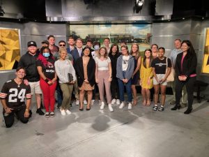 A group of diverse individuals posing together in a studio setting with a backdrop of a building.