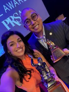 Two people smiling and holding trophies at an awards event.