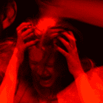 A person with hands in their hair appears distressed, shown in vivid red lighting.