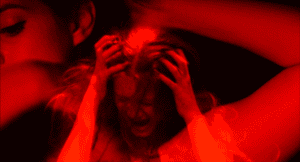 A person with hands in their hair appears distressed, shown in vivid red lighting.