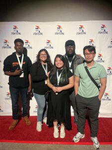 Five people stand on a red carpet in front of a backdrop with "Film Festival" logos. Erica Miyamoto stands in the center