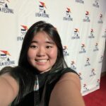 Person taking a selfie on a red carpet with a film festival logo backdrop.