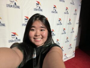 Person taking a selfie on a red carpet with a film festival logo backdrop.