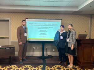 Three people standing in front of a presentation screen titled "Narrative Instruction in Video Game Tutorials" at a conference.