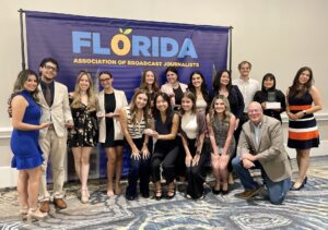 A group of people poses in front of a "Florida Association of Broadcast Journalists" banner, with several holding awards.