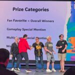 A group of people stand on stage at Full Sail University as prize categories are displayed on a large screen during an award event.