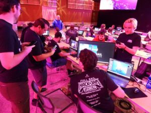 People working on computers at a hackathon event, with multiple screens and participants collaborating in a large indoor space.