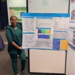 A woman in a green suit stands beside a scientific poster about trends in animal-related deaths, displayed at an academic conference.