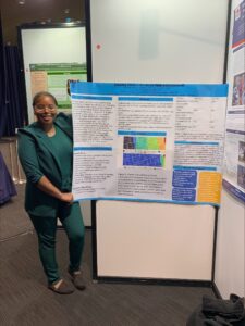 A woman in a green suit stands beside a scientific poster about trends in animal-related deaths, displayed at an academic conference.