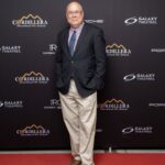 A man in a blazer, dress shirt, and khaki pants stands on a red carpet in front of a Cordillera International Film Festival backdrop.