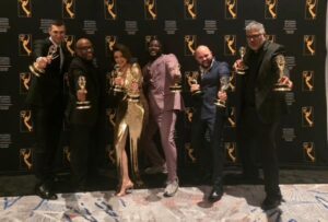 Six people holding Emmy awards pose together in front of a step-and-repeat backdrop with the National Academy of Television Arts & Sciences logo.