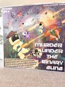 Box cover for "Murder Under the Binary Suns" board game shows cartoon astronauts and spaceships in space, with the game title and a description of the social deduction gameplay.