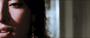 Close-up of a person's face in partial shadow, showing one eye, nose, and mouth, with soft light and a blurred background.