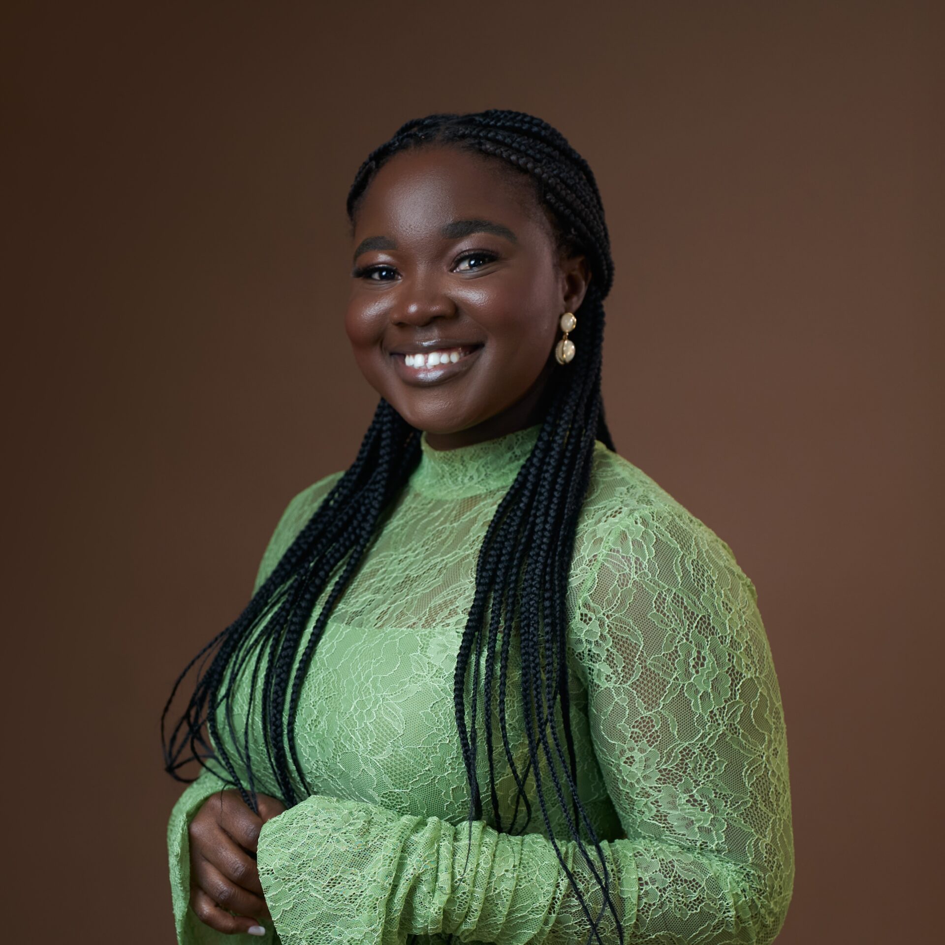 A smiling woman with braided hair wearing a lime green lace top against a brown background.